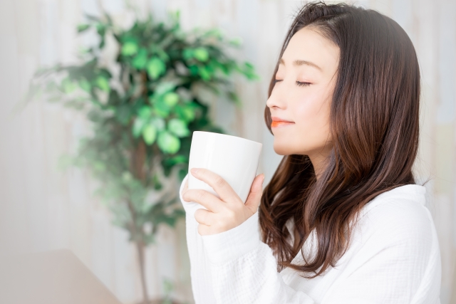 30代または40代の女性が白いカップでカフェインレスコーヒーを自宅で飲んでいる画像